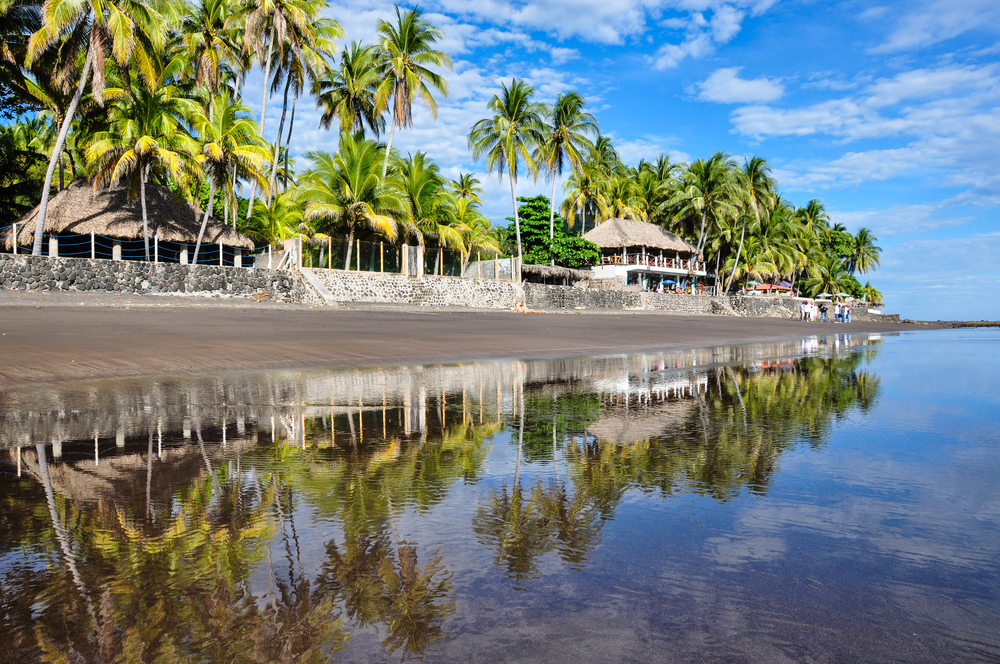 Late afternoon on the ocean in El Salvador pictured with still water leading to the edge of the black-sand beach on a clear day with blue skies above