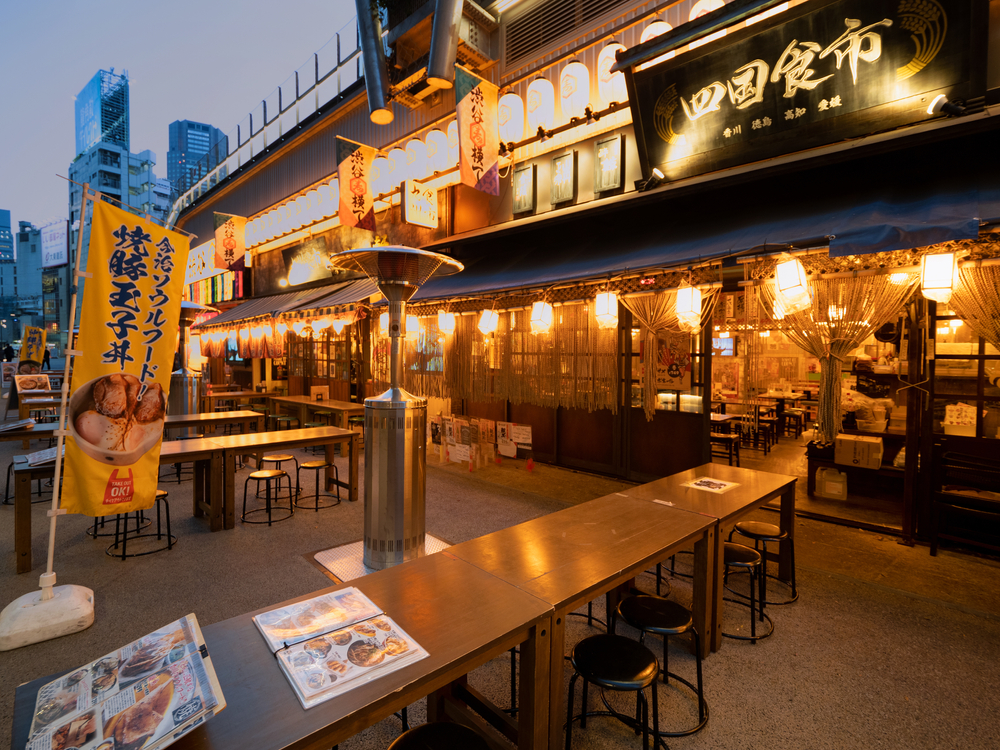 To illustrate the average trip to Tokyou cost, Shibuya Yokocho in Miyashita Park, a Japanese restaurant, illuminated by yellowish lights with outdoor dining option.