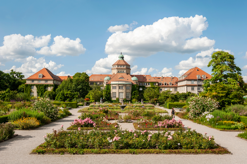 A large old castle that has a botanical garden in its front that has various plants and flowers. 