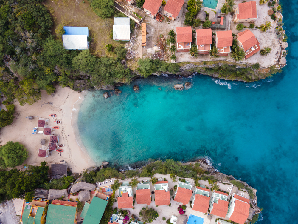 Aerial view on a beach in between a cliff with orange-roof structures. 