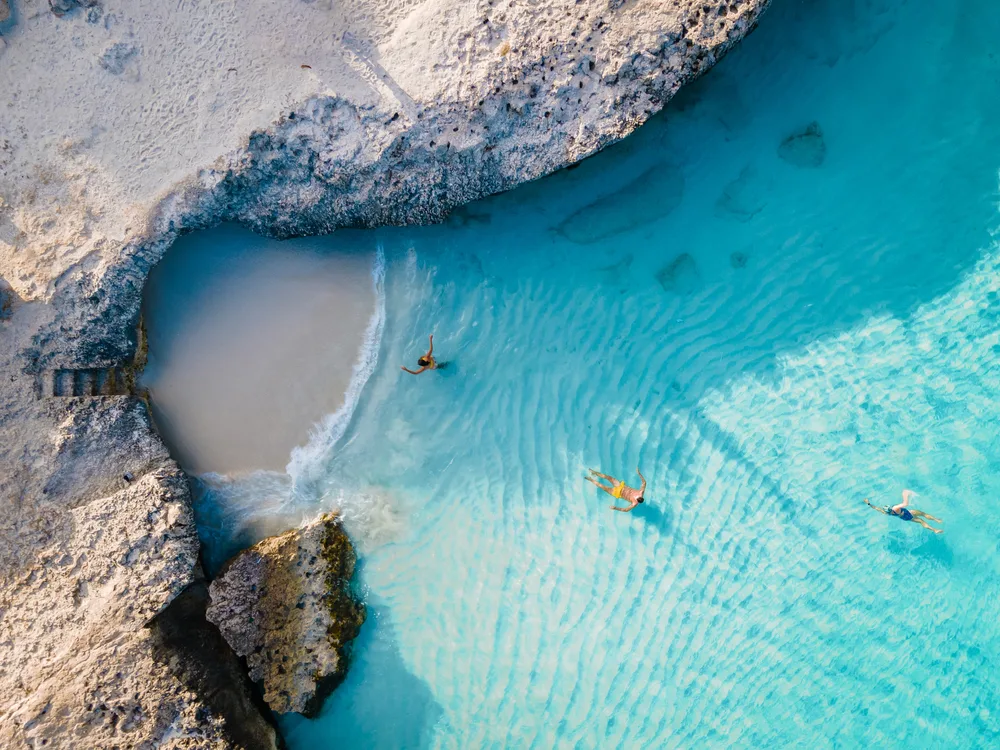 Aerial view on a couple swimming on a crystal clear beach with rocky shore. 