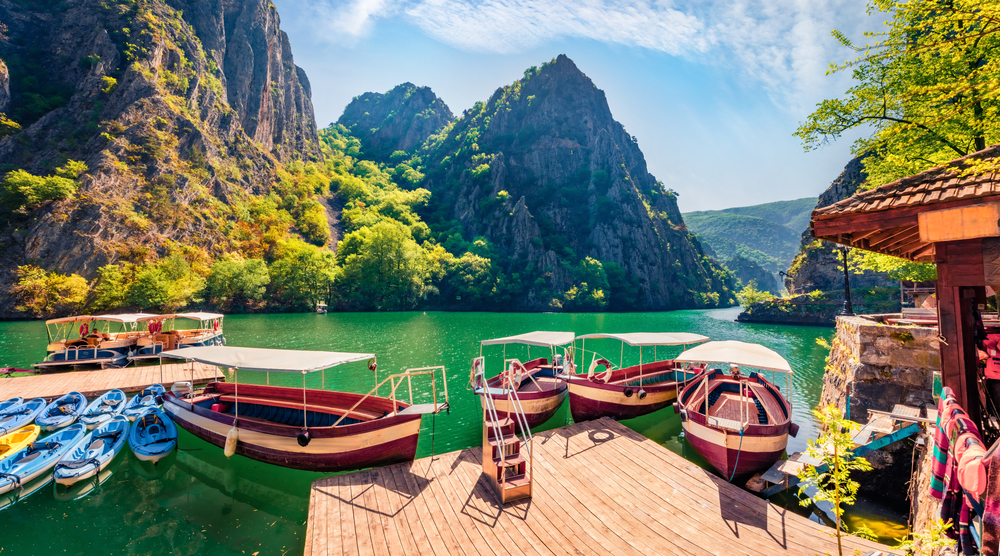 Matka Canyon in North Macedonia shown in springtime with boats on the water and mountains in the distance for a list ranking the top cheap places to travel in Europe