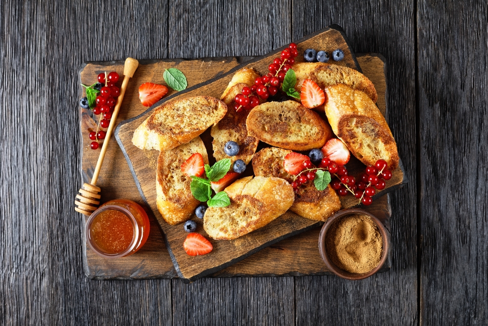 View looking down at wentelteefjes, or Dutch French toast, with berries and fruit served with honey and syrup on a list of the best Dutch food to try
