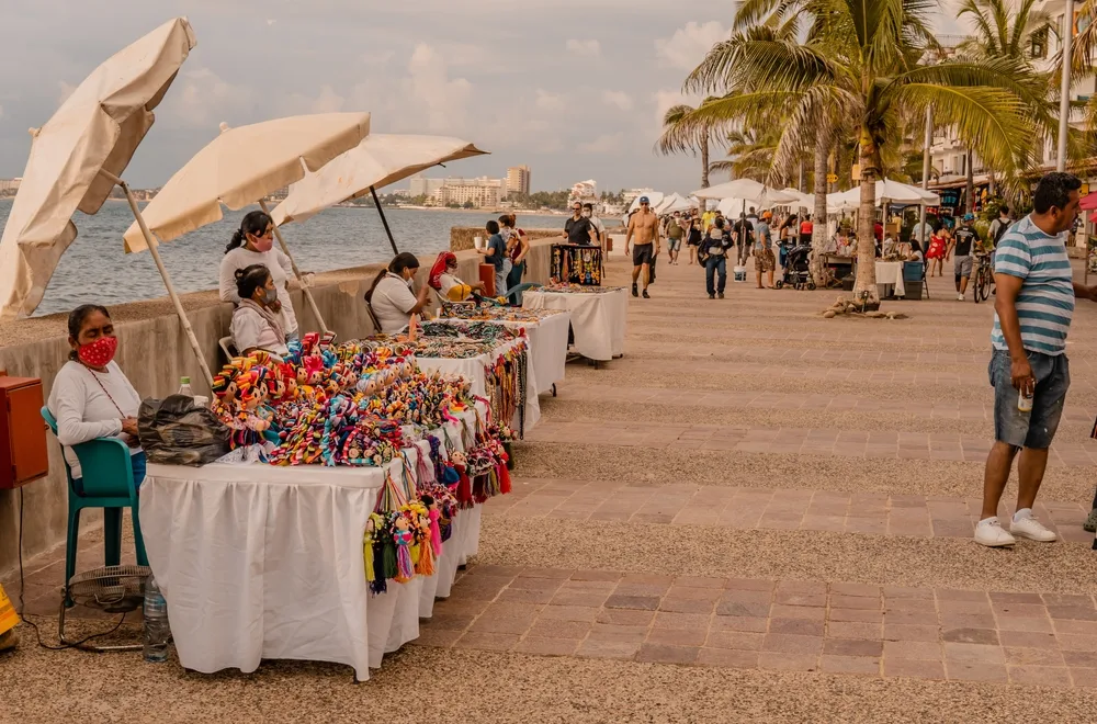 Local vendors selling souvenirs on the side of a bay walk, while tourist pass by.