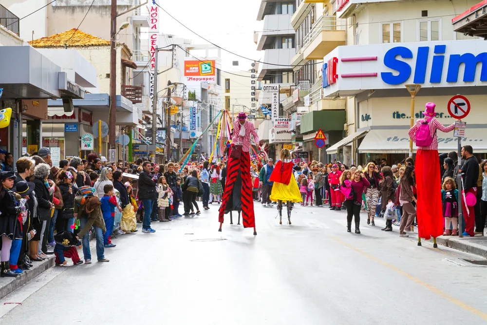 A busy day on a street where performers are seen walking on stilts while the crowd watch them on the side of the street. 