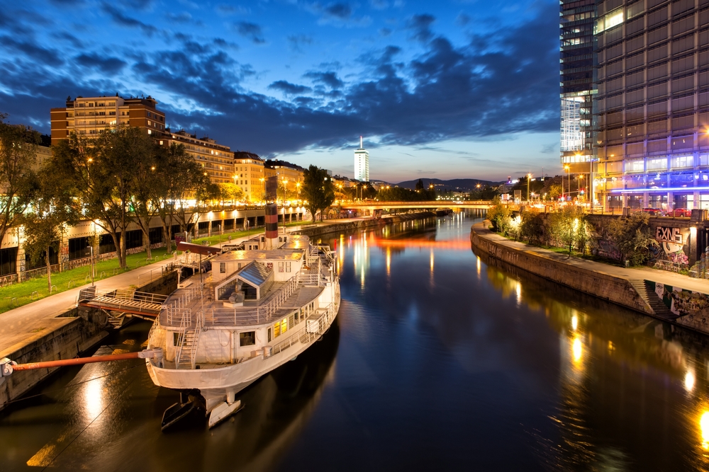 A boat is docked on the side of a calm canal at night. 