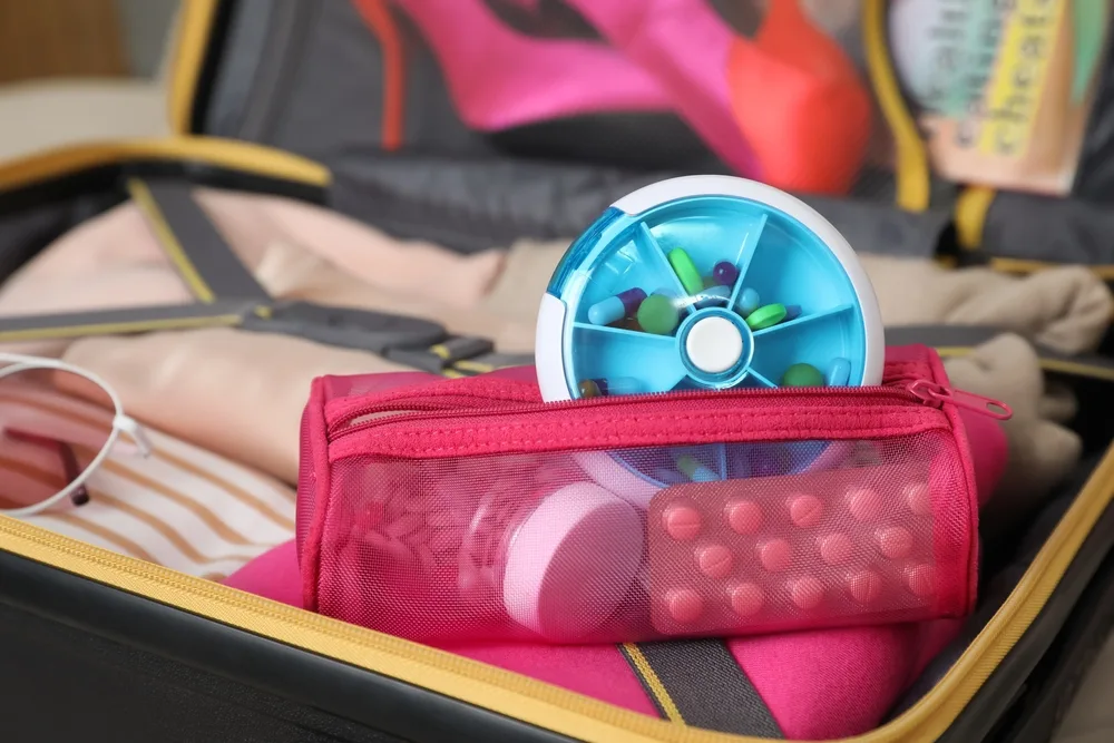 A pink pouch with vitamins and medications in a pill organizer being placed in checked baggage for a guide showing how to fly with vitamins according to TSA rules