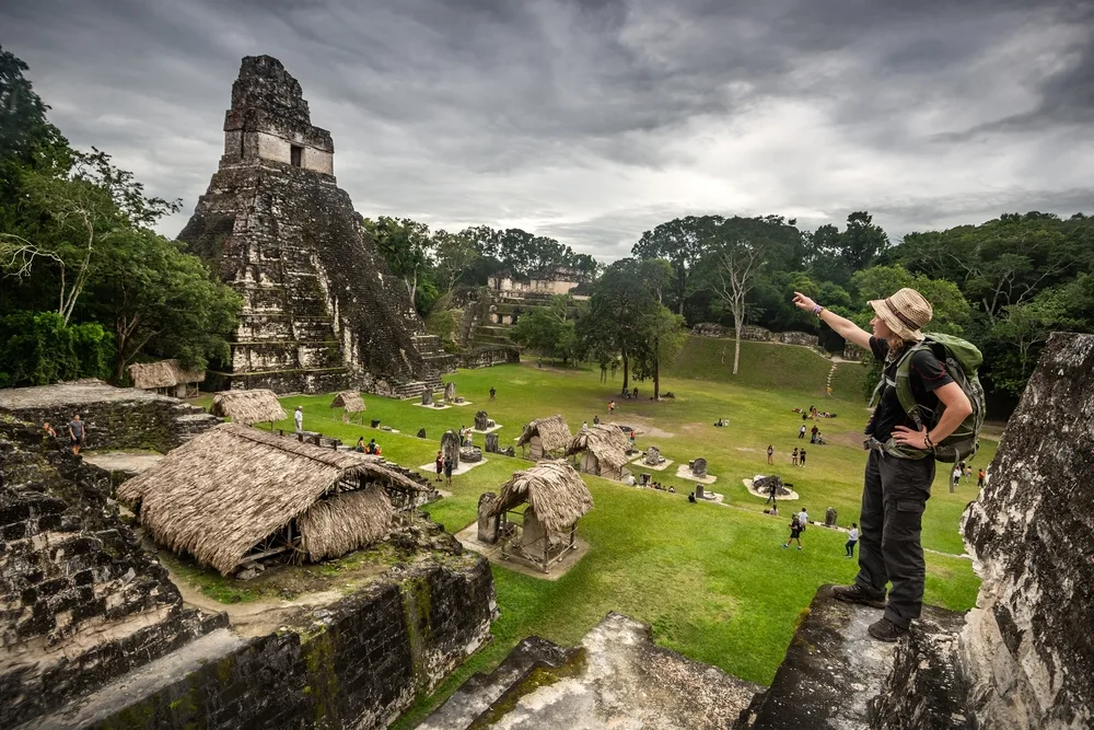 Woman standing at the famous Tikal Pyramid (for a guide to the average Guatemalan vacation cost) on an overcast day