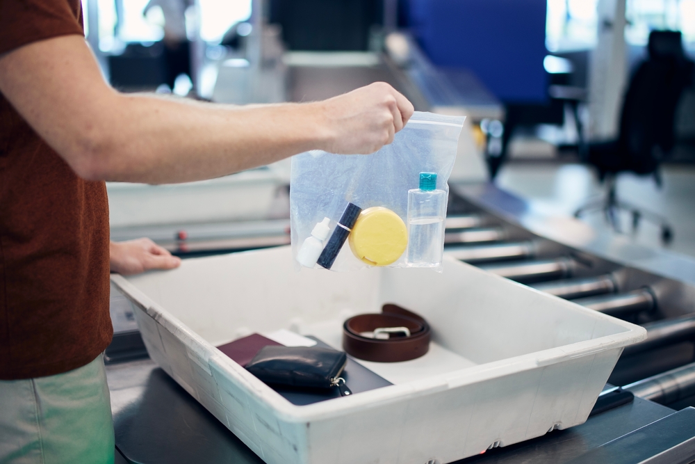 Man places a clear bag with liquids and vitamins into a tray at a TSA checkpoint at the airport as he flies with vitamins