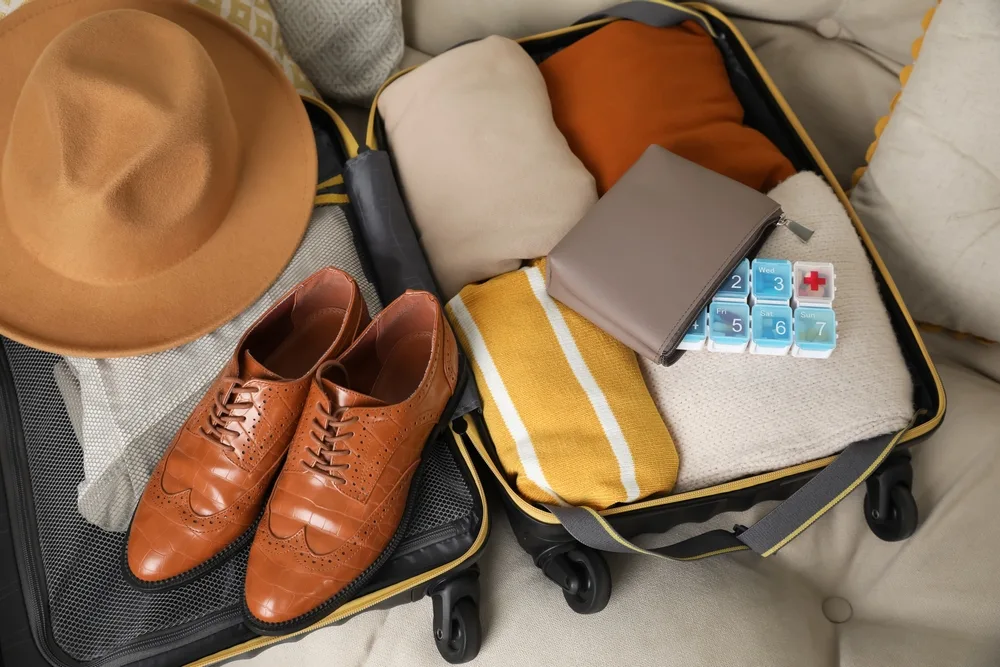 Neatly packed man's suitcase with shoes, hat, clothes, and a pill organizer to show the concept of how to fly with vitamins in your checked baggage