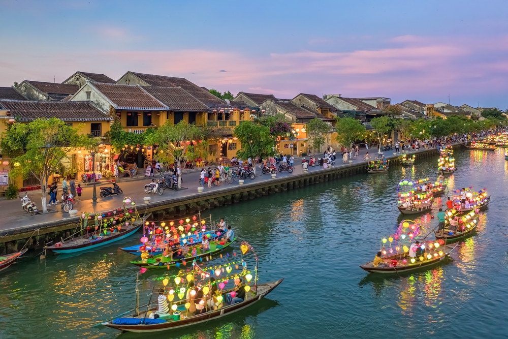 Rickety boats float on a canal in Hoi An, as seen at dusk with lanterns on them, for a piece titled Average Trip to Vietnam Cost