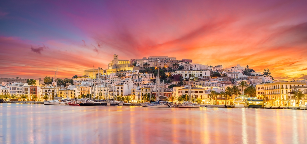 Eivissa (Ibiza) Spain lit up at dusk reflecting on the water for a list of the best trips for friend groups