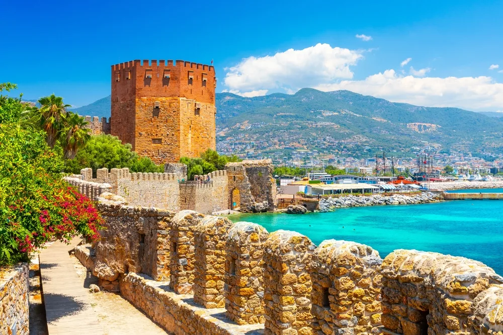Harbor of Alanya on a gorgeous summer day pictured with teal water lapping the coast with a stone wall on either side