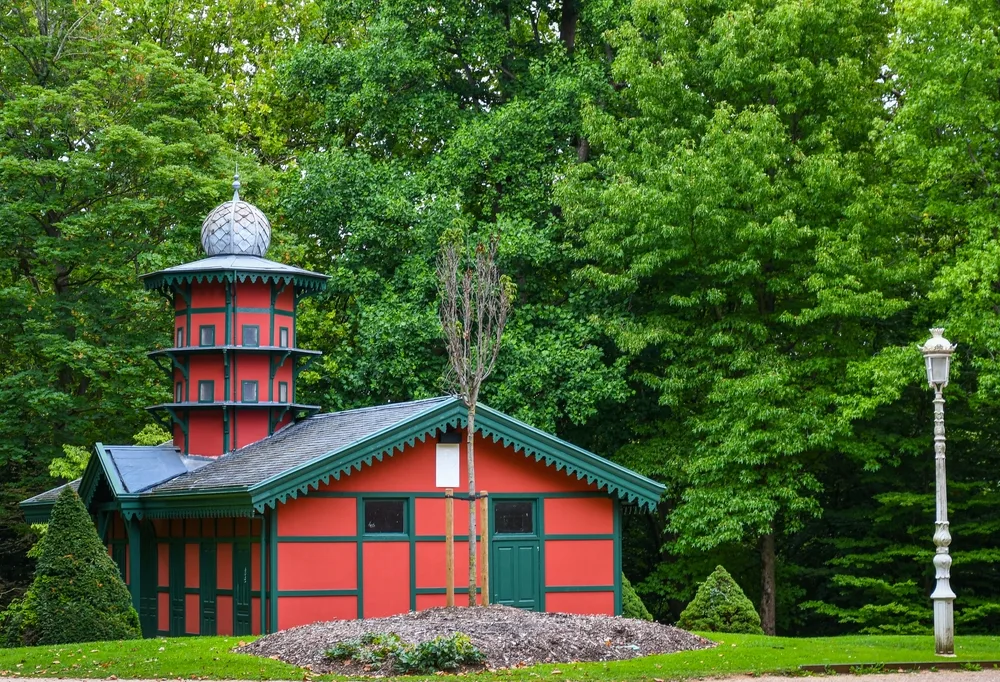 A bright red painted on house surrounded by green grass and many trees.