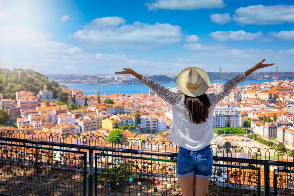 A women spreading her arms in the air while facing a city at a distance. 