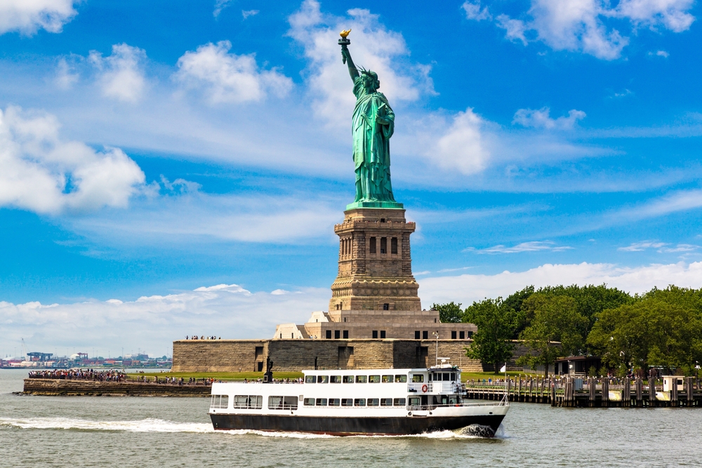 White ferry making its way across the water in front of the Statue of Liberty as an image for a guide to the average trip to New York City cost