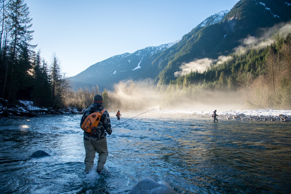 Fly fisherman casting with friends in a river by the mountains for a list ranking the top places for a guys trip