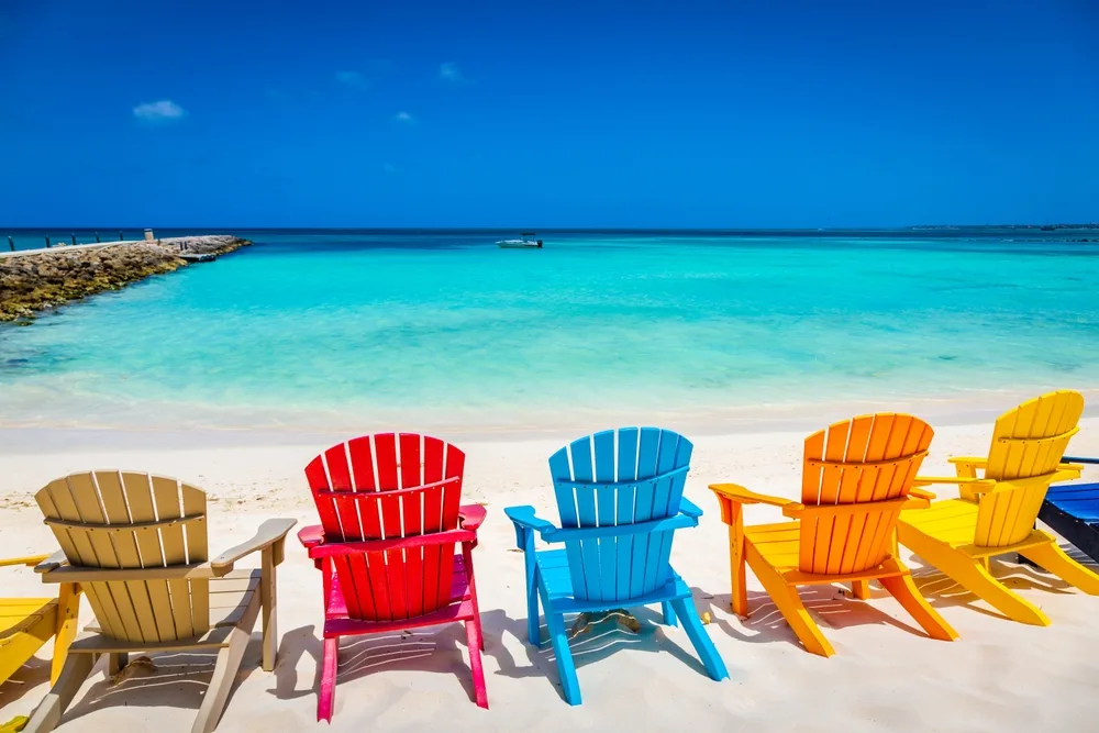 Vibrant wooden chairs on a fine white beach face the calm and clear beach. 