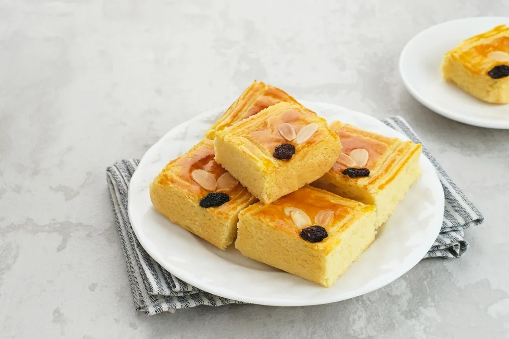 Traditional Dutch food butter cake or boterkoek sliced into squares and served with sliced almonds and blueberries on top on a white plate resting on a partnered napkin