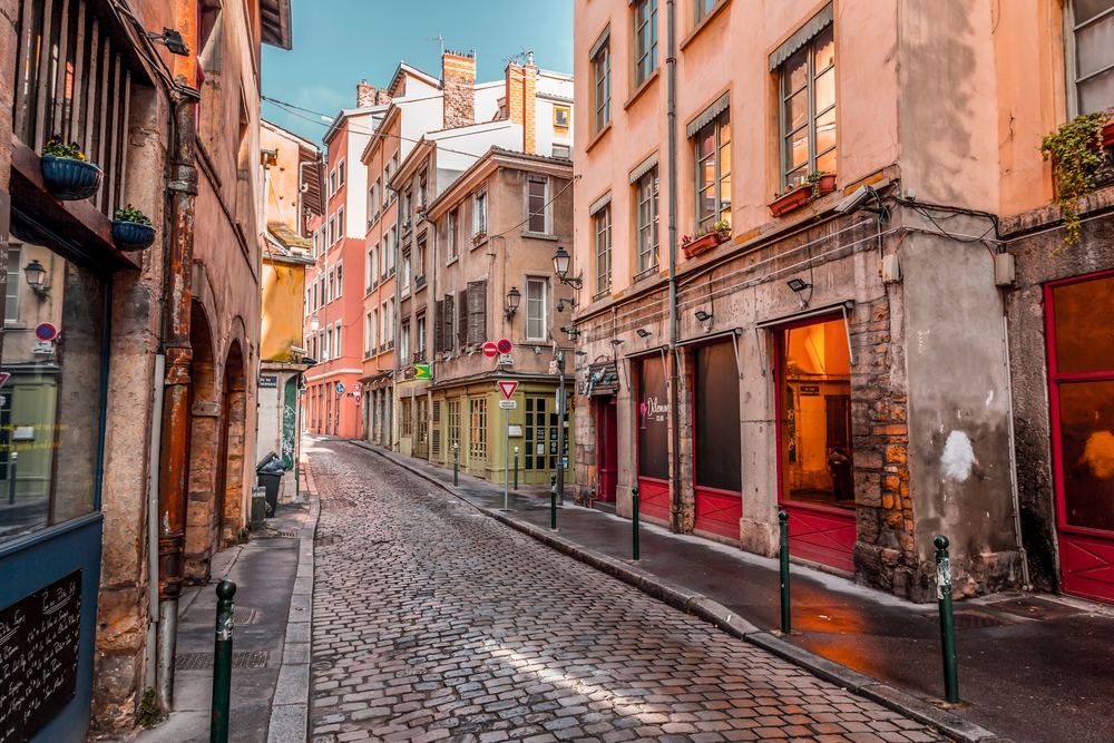 Photo of a cobblestone street pictured between old yellow and pink buildings during the cheapest time to visit Lyon