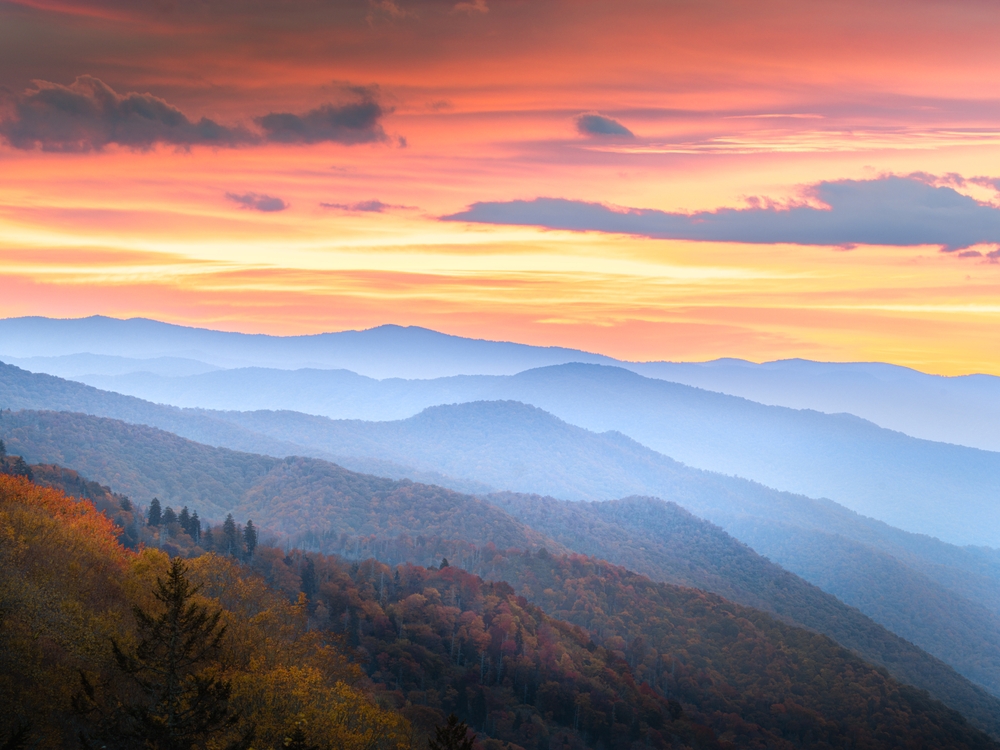 A sunset over a vast forest on a misty mountain during an autumn season, a section image for an article about trip cost to Pigeon Forge.