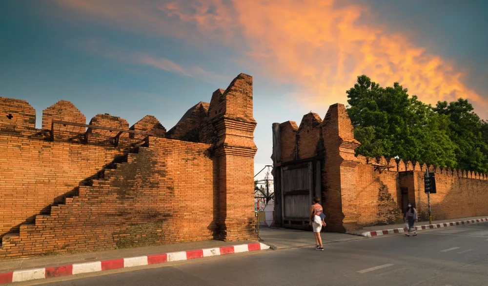 A tourist is walking towards a gigantic gate structure during sunset. 