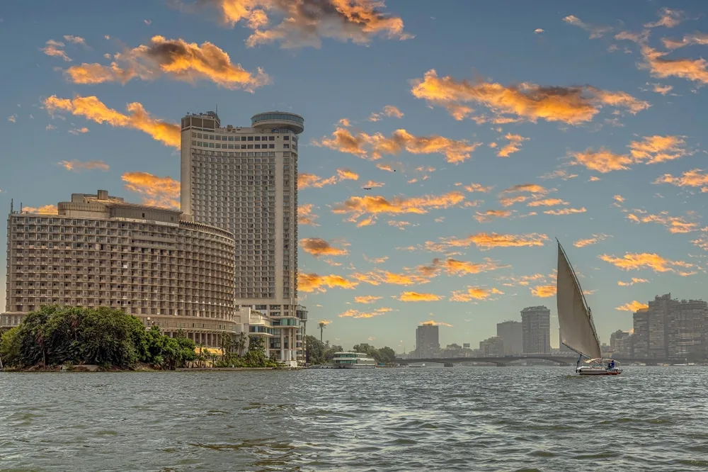 Two large structures on the side of the river, photographed during a sunset for a piece on where to stay in Cairo, and on the river is a sailboat.
