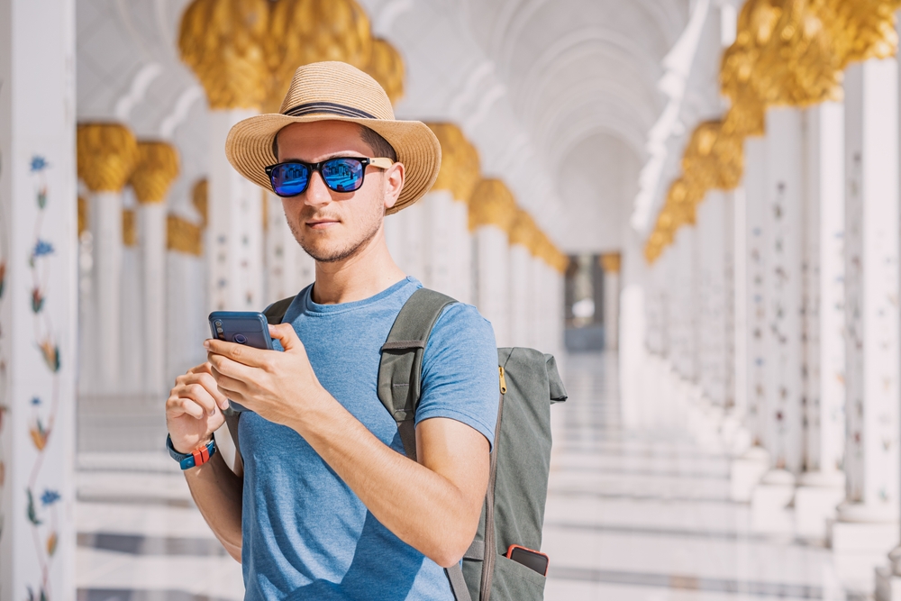 Man standing in the Great Mosque of Sheikh Zayed in Abu Dhabi uses his smartphone for an article explaining how much does it cost to text internationally