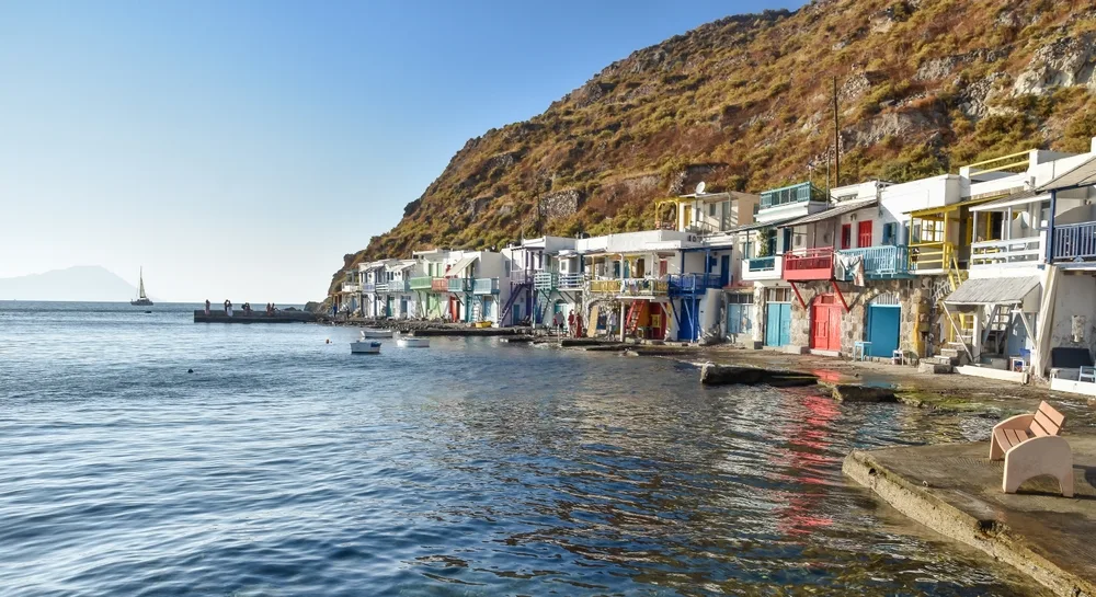 A small fishing village with small houses and rearing a cliff, an image for a travel guide about safety in visiting Milos.