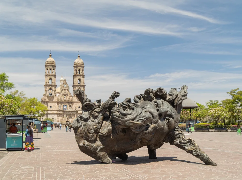 Photo of a statue and cathedral in Zapopan pictured on a semi-cloudy day for a guide to where to stay in Guadalajara