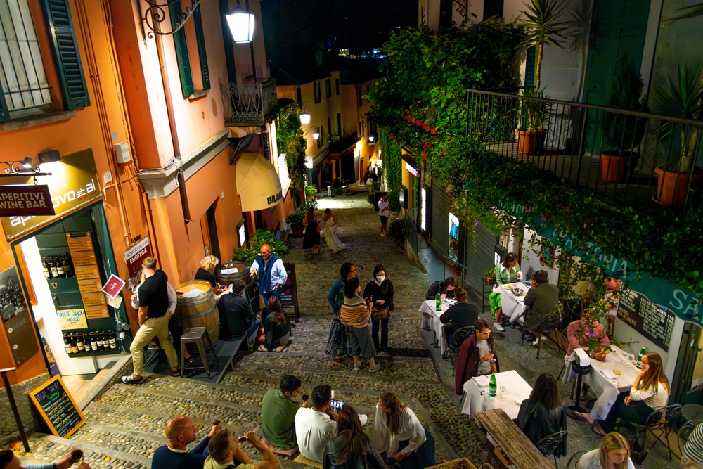 A view on a steep street with restaurant tables and people enjoying their time in the evening. 