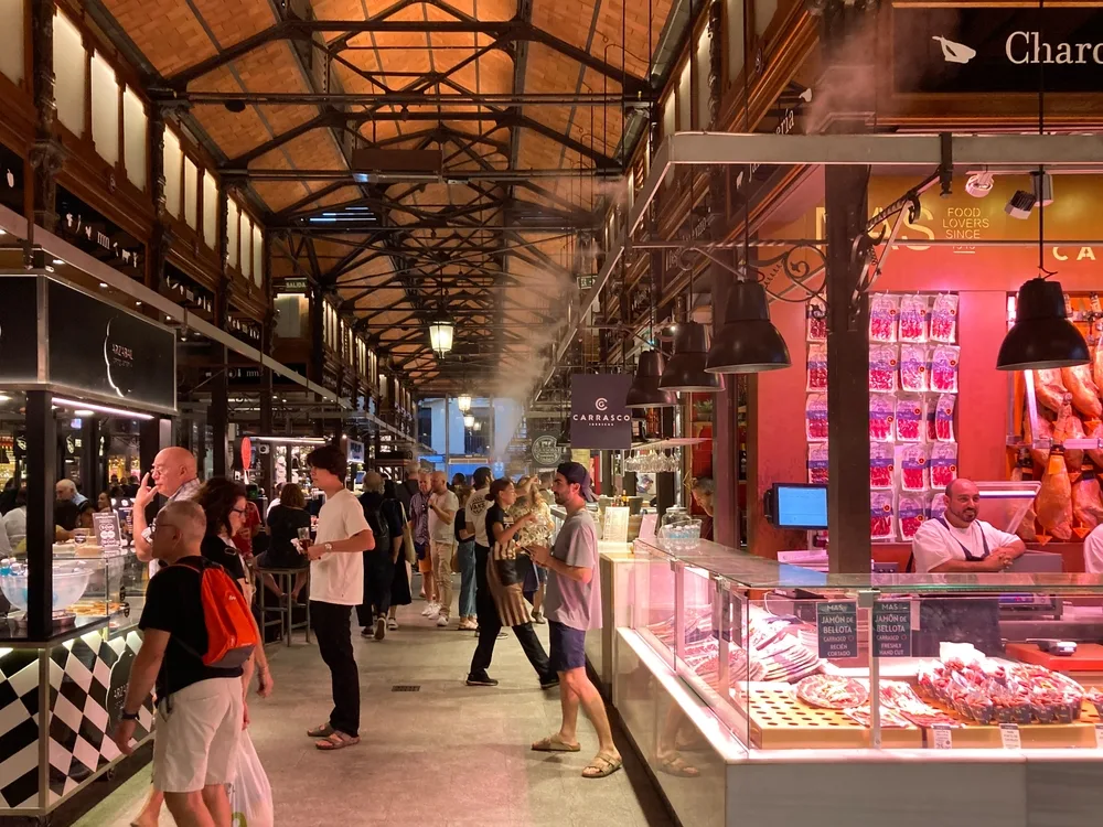 People checking out the stores in the Mercado San Miguel Food Market where various food items are displayed in each store, an image for a travel guide about safety in visiting Madrid.