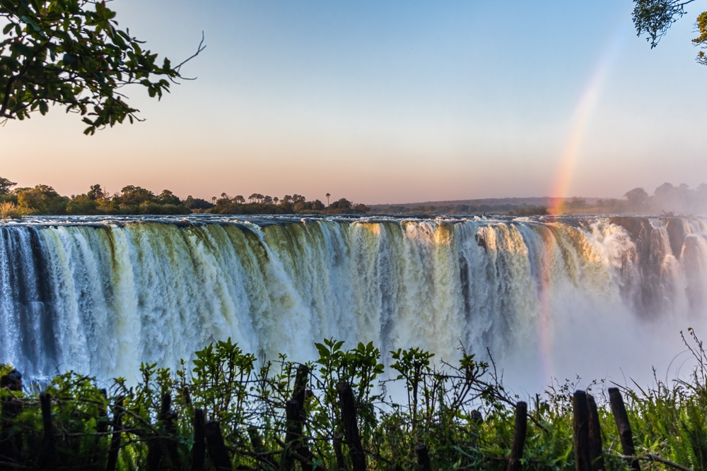 A large waterfalls with a rainbow where water is seen flowing nonstop in large volume. 
