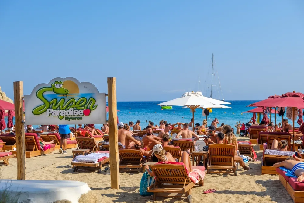 Mykonos is one of the top Greek party islands, shown with tourists at Super Paradise Beach Club as people sunbathe and mingle on the beach