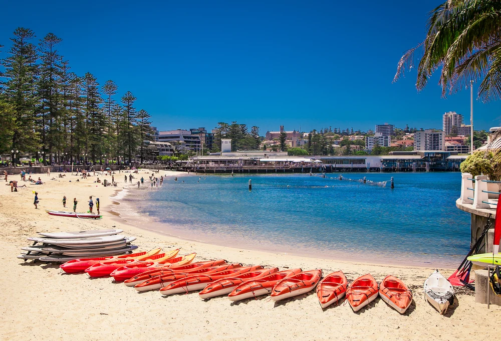 Red kayaks lie on the bright white sandy beach in Manly, one of the best areas to stay when in Sydney
