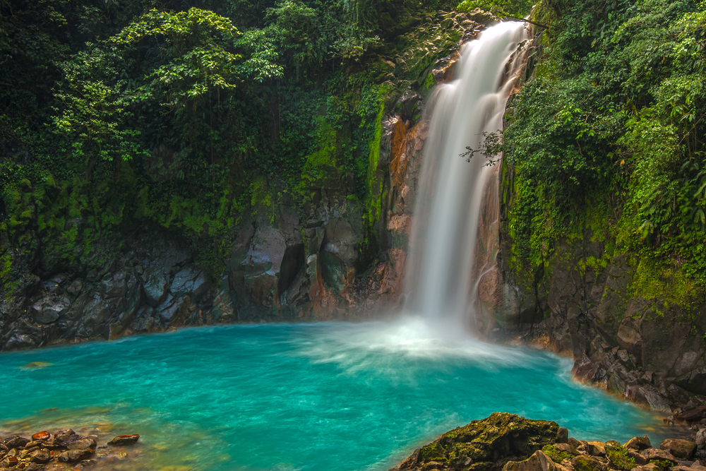 Rio Celeste waterfall in La Fortuna, Costa Rica shown with a blue pool at the base in the jungle for a list of the best trips for groups of friends to take