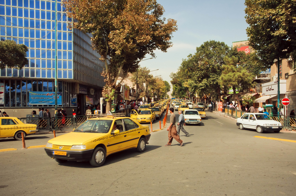 Yellow cabs driving down the street with people walking aroun in Sanandaj during the worst time to visit Iran, early winter