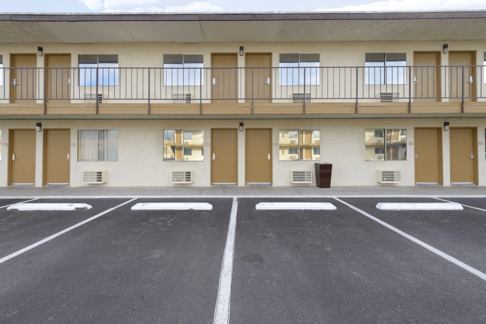 Two story motel facade with parking lot in view and beige coloring on the exterior to show what a motel is