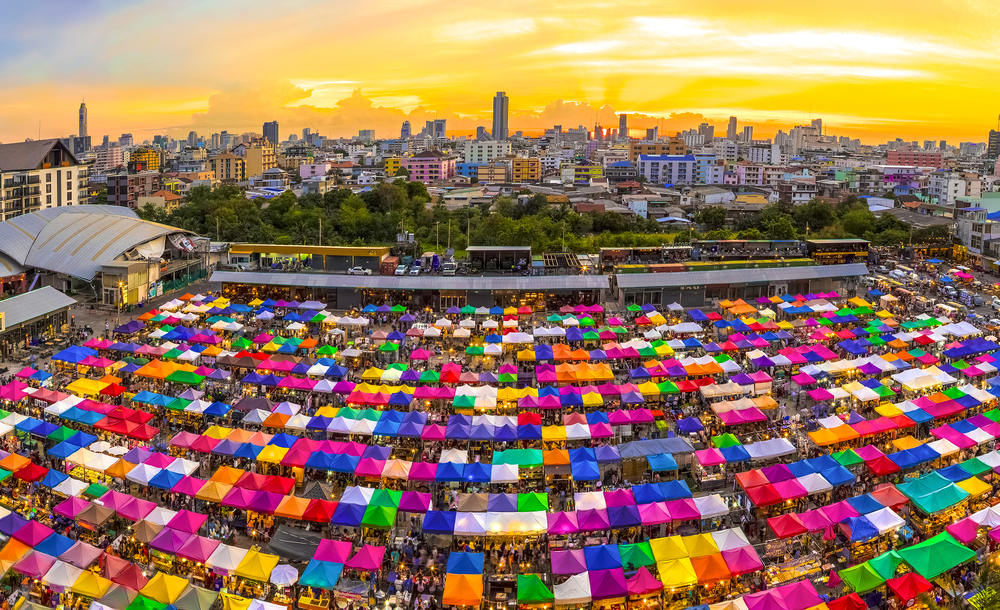Multi-colored tents at a weekend market shown in front of the Bangkok skyline at sunrise for a list of the best places for solo travelers