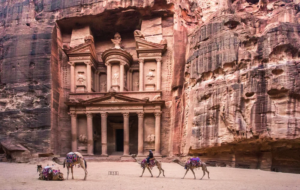 The Treasury carved in sandstone rock in Petra, Jordan shown with camels and people in front for a list of the best tourist destinations in the world