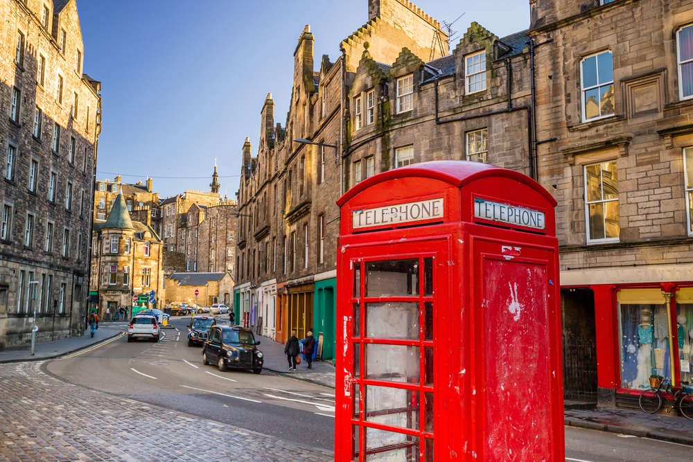 As a featured image for a guide titled Is It Safe to Visit Edinburgh, a view of the Royal Mile and its unique red phone booth in the foreground pictured up-close