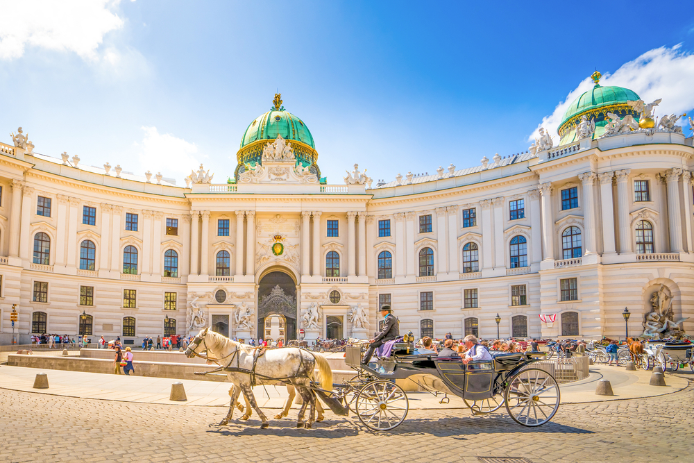 Tourists riding a horse carriage in a town circle in front of a historical building during sunny mid day. 