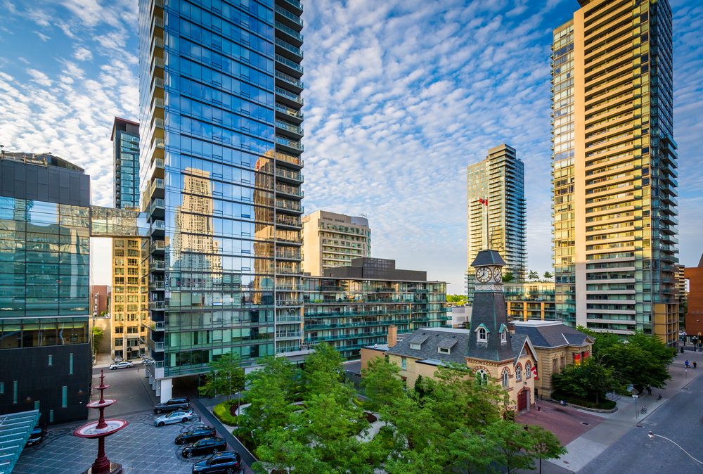 A historical structure with clocks on its tower in Yorkville and Midtown, which has a small park beside it is surrounded by tall modern skyscrapers, one of our picks on the best areas to stay in Toronto.
