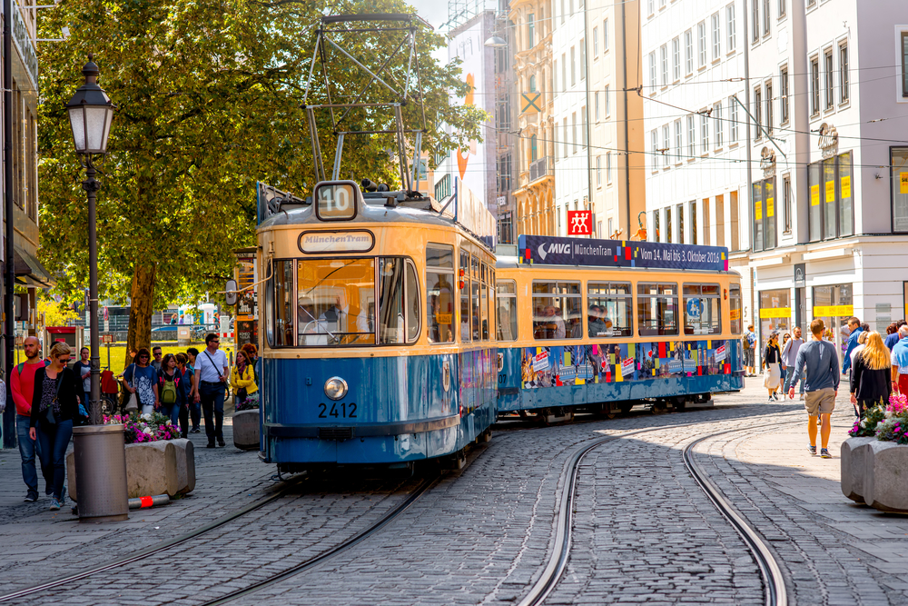 A yellow and blue tram running in the middle of the city, where people are seen walking outside its rails. 