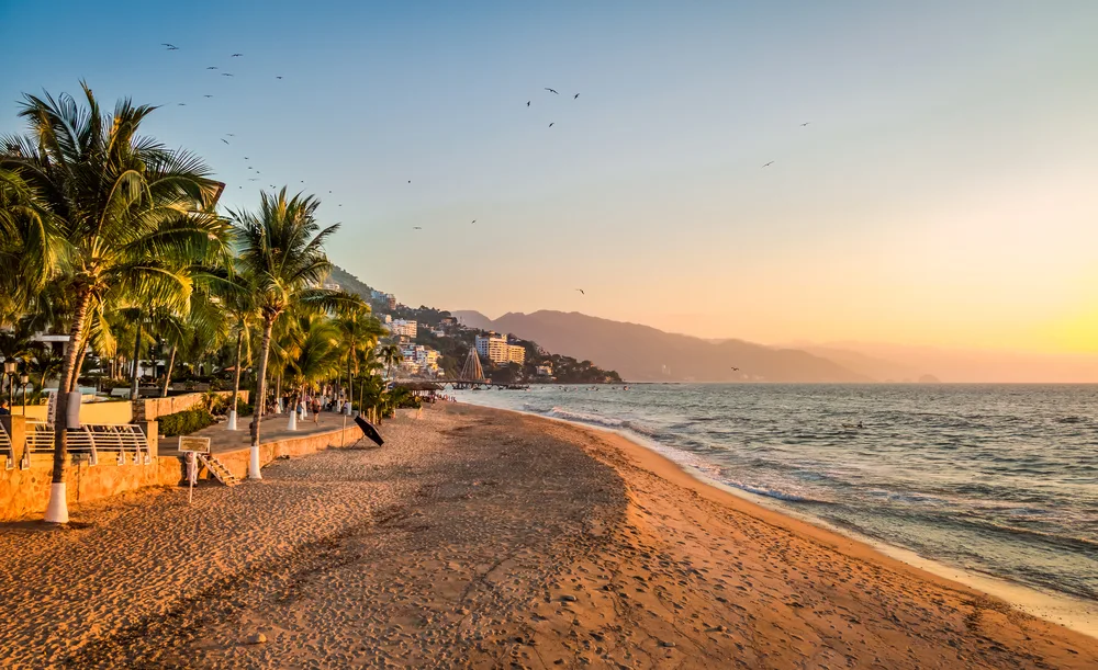 Amazing sunset in Puerto Vallarta pictured with rich brown sand being lapped by waves in the ocean