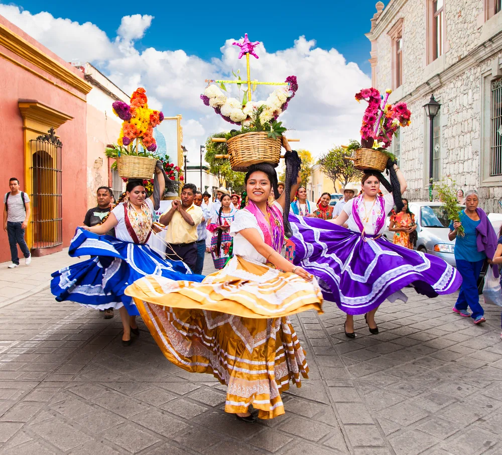 Local women dressed in vibrant clothing as they dance through a street in celebration of a festival.