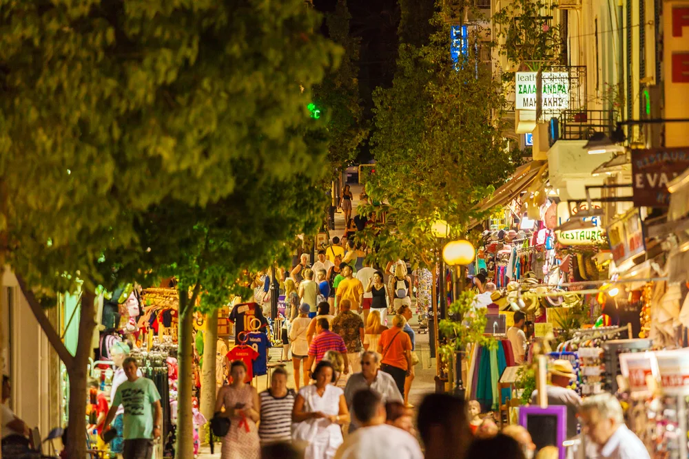 A crowded street at night with row of small stores selling souvenirs operating on both sides of the street, an image for a travel guide about safety in visiting Crete.