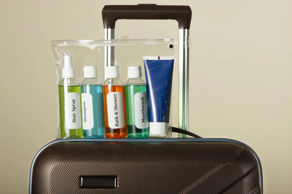 Cosmetics and toiletries in TSA-approved clear bag sitting on black luggage shows the requirements in the carry on liquid guide