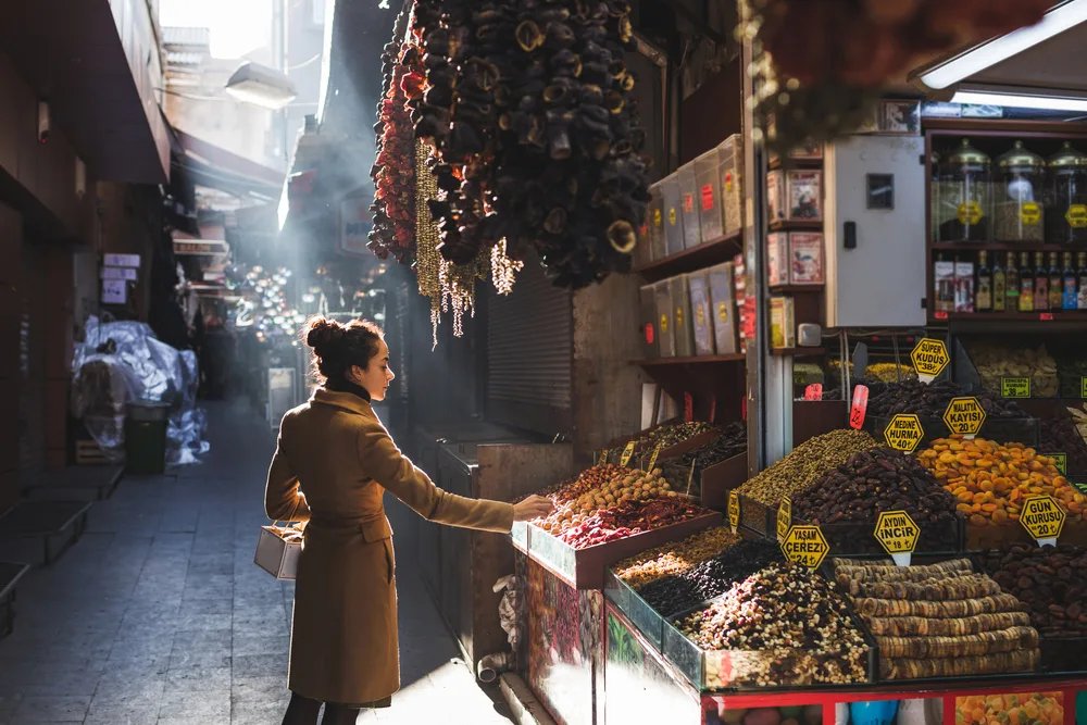 Woman in a tan trench coat pictured looking at nuts in an open-air market in the late fall in Istanbul