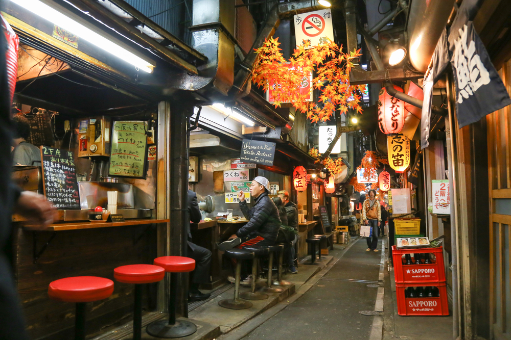 A narrow alley with traditional Japanese restaurants where people are seen eating. 